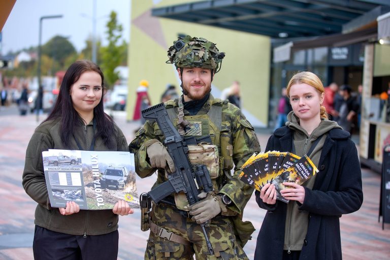 Tři lidé před budovou s propagačními materiály armády