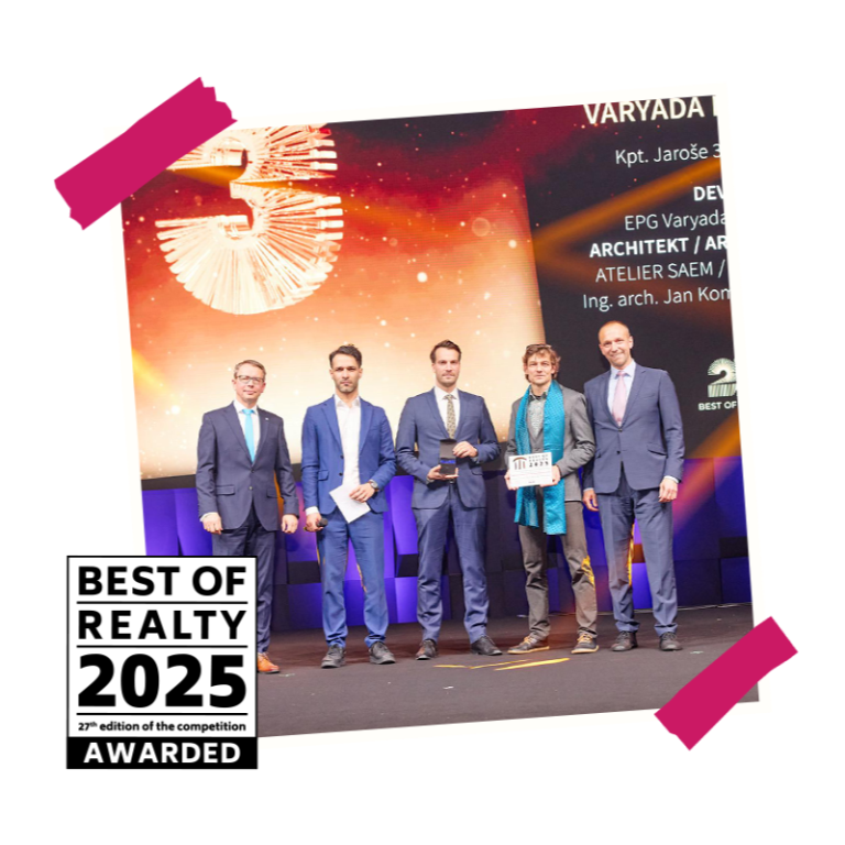 Skupina lidí v oblecích na pódiu s oceněním Best of Realty před velkým displejem.