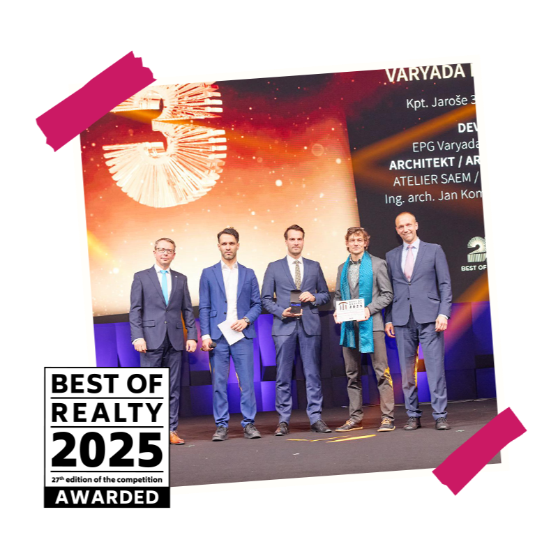 Skupina lidí v oblecích na pódiu s oceněním Best of Realty před velkým displejem.