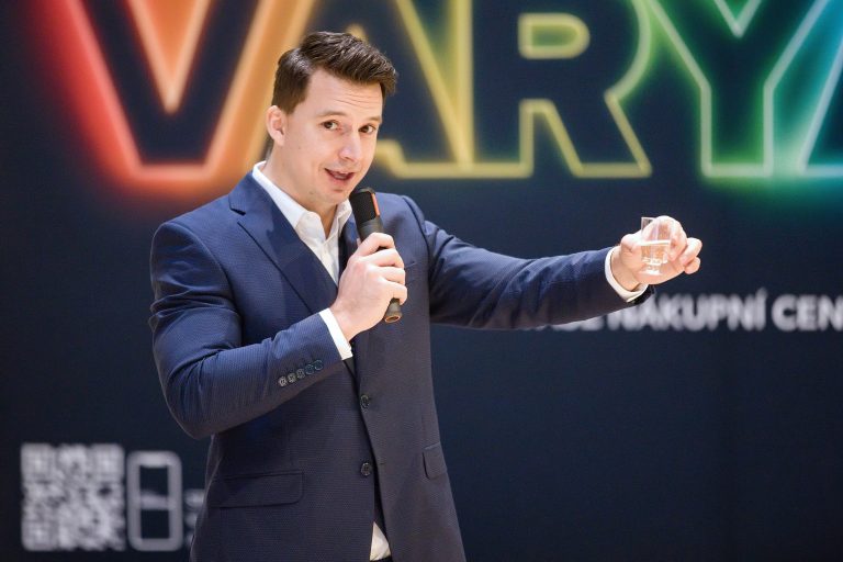 Muž v modrém obleku mluví do mikrofonu na pódiu