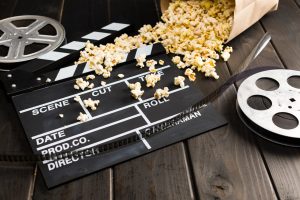 Filmová klapka, rozlitý popcorn a filmový kotouč na stole